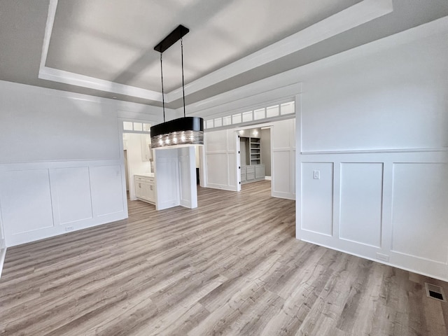 unfurnished dining area with light wood-type flooring and a raised ceiling