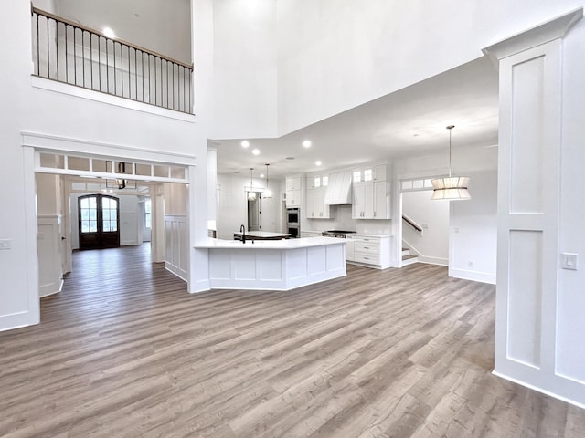 kitchen with white cabinets, a towering ceiling, light hardwood / wood-style flooring, and pendant lighting