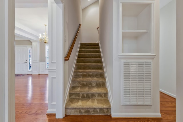 stairway with wood-type flooring and a notable chandelier