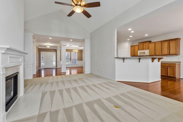 unfurnished living room featuring light hardwood / wood-style floors, a fireplace, ceiling fan with notable chandelier, ornamental molding, and decorative columns