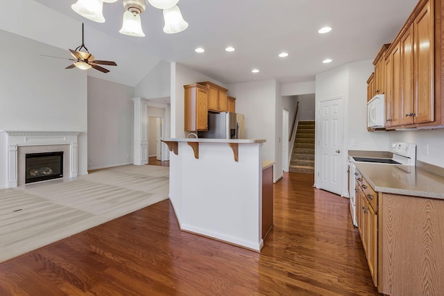 kitchen with white appliances, lofted ceiling, a kitchen bar, wood-type flooring, and ceiling fan