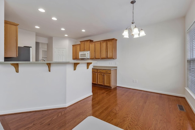 kitchen with light hardwood / wood-style floors, kitchen peninsula, a breakfast bar area, and stainless steel refrigerator