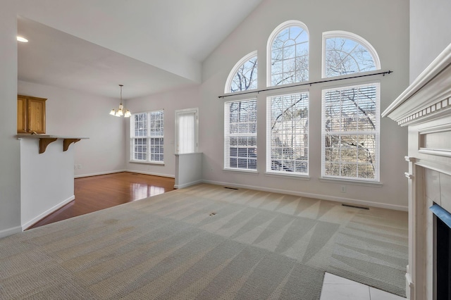 unfurnished living room featuring light carpet, high vaulted ceiling, an inviting chandelier, and a fireplace