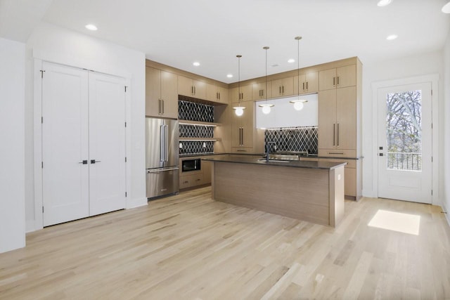 kitchen with high end fridge, a center island with sink, light wood-type flooring, and decorative light fixtures