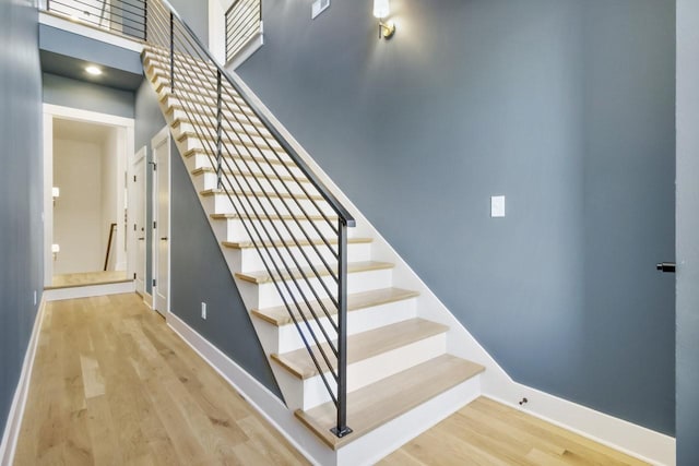 stairs with a towering ceiling, baseboards, and wood finished floors