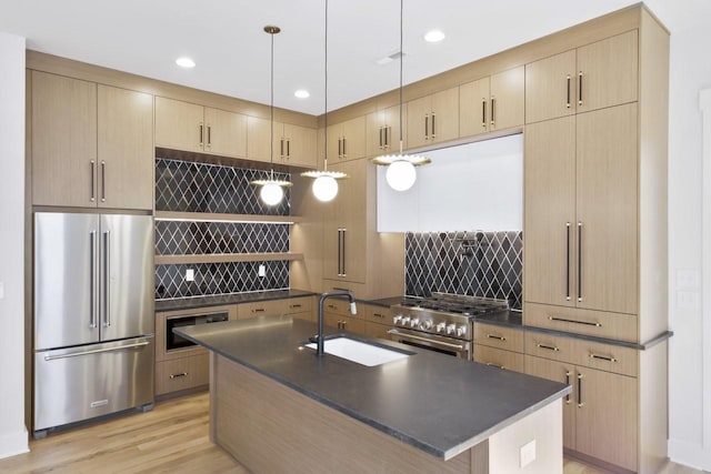 kitchen with sink, light brown cabinets, high quality appliances, an island with sink, and pendant lighting