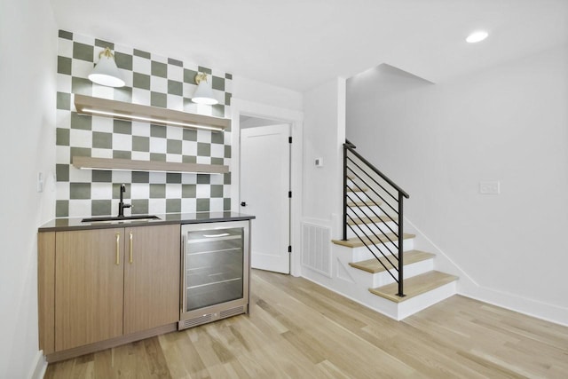 bar with sink, beverage cooler, light wood-type flooring, and decorative backsplash