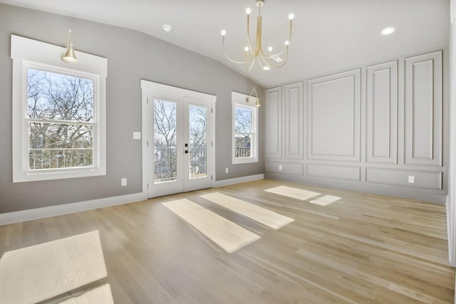 interior space with an inviting chandelier, vaulted ceiling, french doors, and light hardwood / wood-style flooring