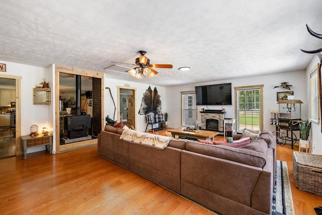 living room with ceiling fan, a wood stove, a fireplace, a textured ceiling, and light hardwood / wood-style floors