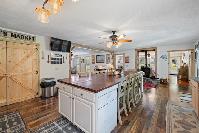 kitchen with a textured ceiling, white cabinets, wood counters, dark hardwood / wood-style flooring, and a wood stove