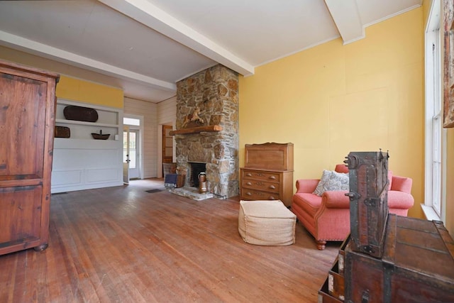 living room with hardwood / wood-style flooring, beam ceiling, and a stone fireplace