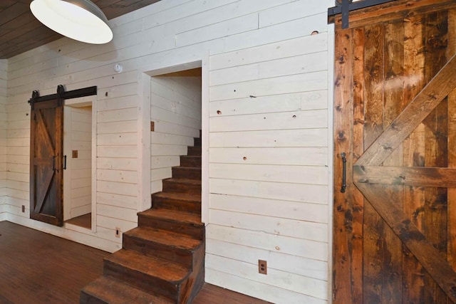 stairs featuring a barn door, wooden walls, and hardwood / wood-style floors