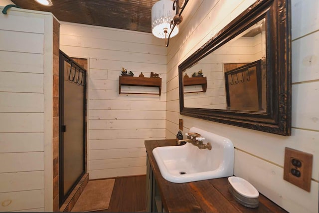 bathroom with a shower with shower door, vanity, and wooden walls