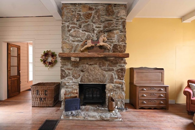 living room featuring wood-type flooring, wooden walls, beamed ceiling, and a stone fireplace