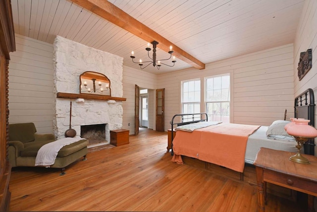 bedroom featuring light wood-type flooring, beamed ceiling, wood walls, and a stone fireplace