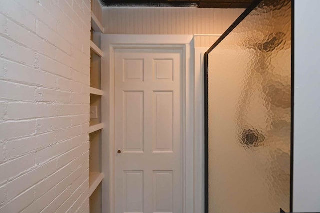 bathroom with a shower with shower door and brick wall