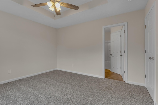 empty room with light colored carpet, ceiling fan, and a raised ceiling