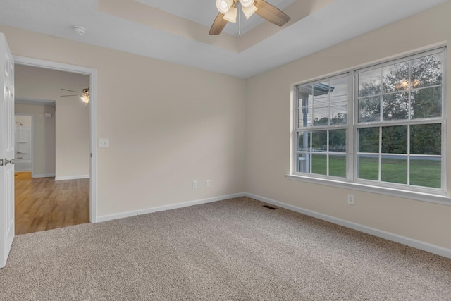 carpeted empty room with ceiling fan, plenty of natural light, and a tray ceiling