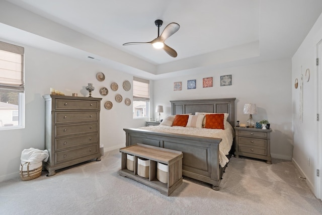 carpeted bedroom with a raised ceiling and ceiling fan