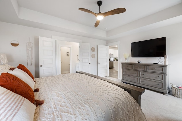 carpeted bedroom featuring a tray ceiling, stainless steel fridge, ensuite bath, and ceiling fan