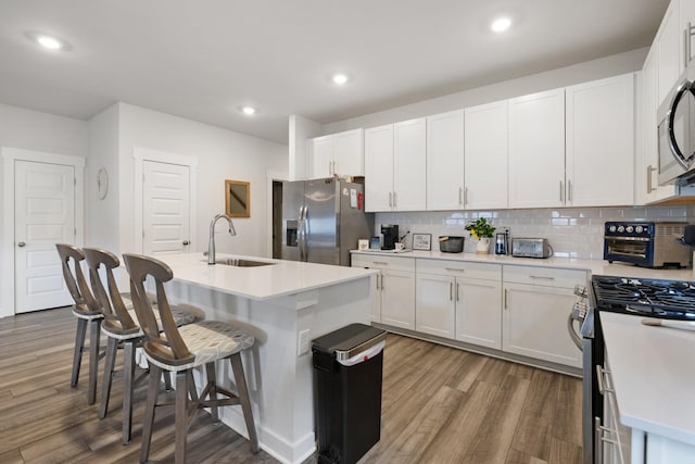 kitchen featuring sink, appliances with stainless steel finishes, white cabinetry, backsplash, and an island with sink