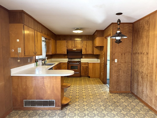 kitchen with range, hanging light fixtures, sink, kitchen peninsula, and wood walls