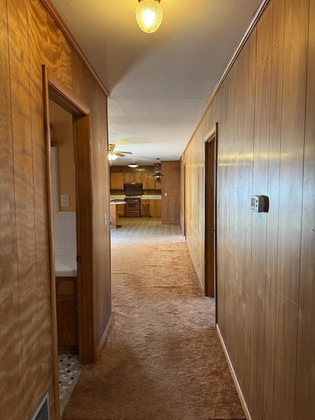 corridor with light carpet, wooden walls, and ornamental molding