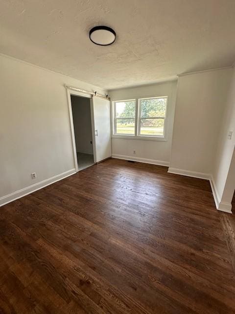 spare room featuring a barn door and dark wood-type flooring