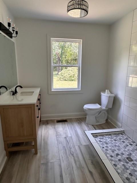 bathroom with hardwood / wood-style flooring, toilet, walk in shower, and vanity