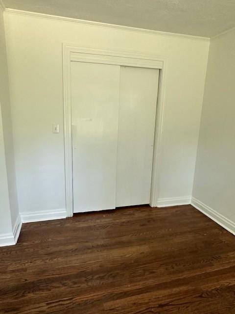 unfurnished bedroom with a closet, crown molding, and dark wood-type flooring