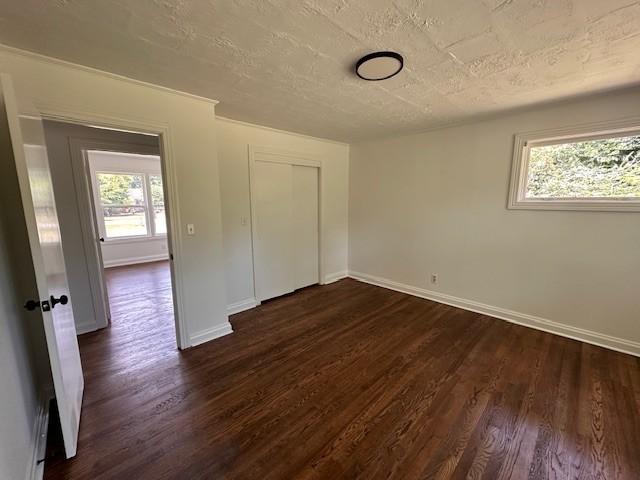 unfurnished bedroom with a textured ceiling, dark hardwood / wood-style flooring, and a closet