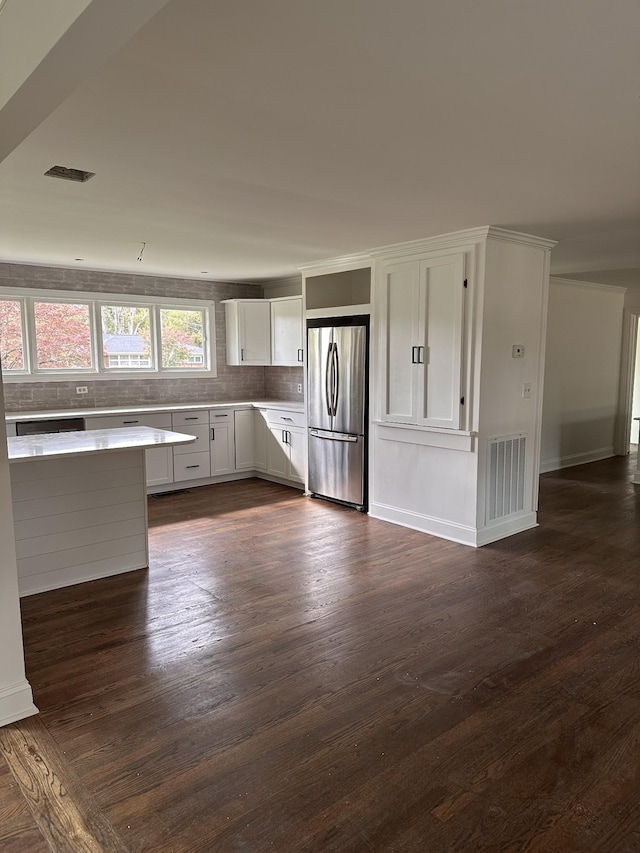 kitchen with backsplash, dark hardwood / wood-style flooring, white cabinetry, and stainless steel refrigerator