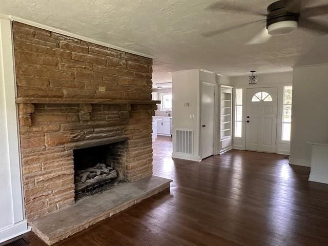 foyer entrance with ceiling fan, dark hardwood / wood-style flooring, a stone fireplace, a healthy amount of sunlight, and a textured ceiling