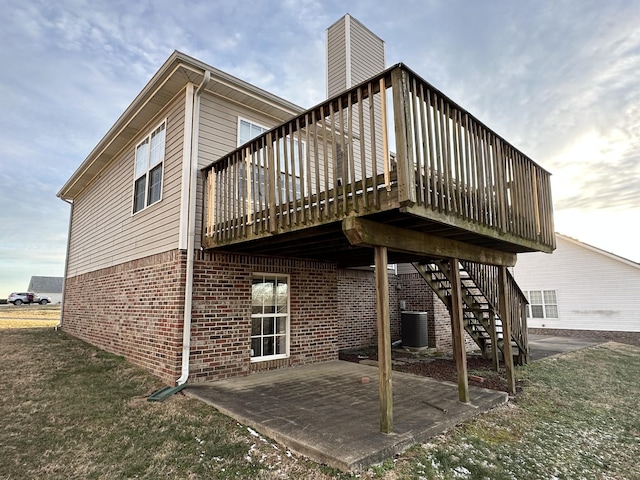 rear view of house featuring a wooden deck, cooling unit, a lawn, and a patio