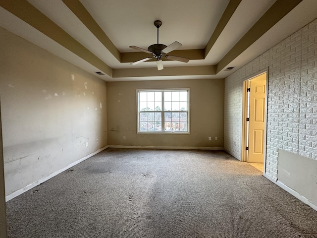 spare room featuring ceiling fan, brick wall, a raised ceiling, and light carpet