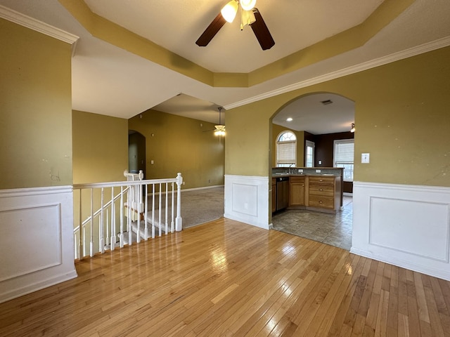 empty room with ceiling fan, light hardwood / wood-style floors, a tray ceiling, and ornamental molding