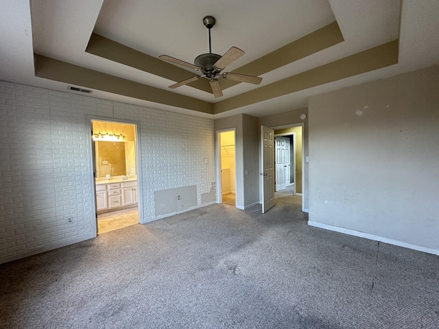 unfurnished bedroom with connected bathroom, brick wall, ceiling fan, and a raised ceiling