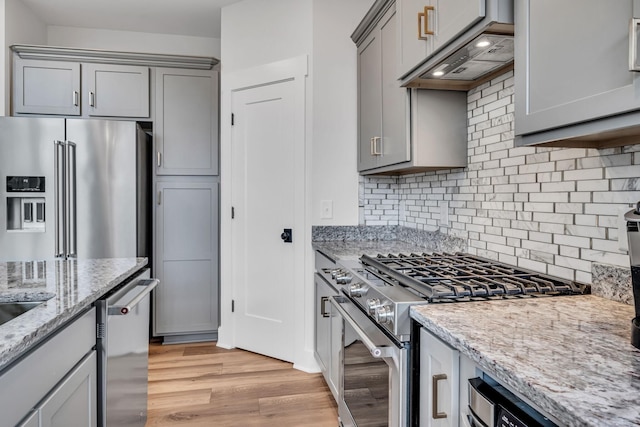 kitchen with light stone countertops, high end appliances, light hardwood / wood-style floors, backsplash, and gray cabinetry