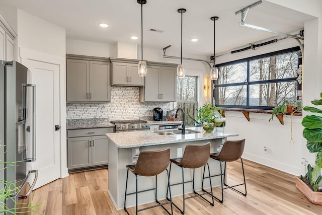 kitchen with pendant lighting, sink, gray cabinetry, light stone counters, and stainless steel appliances