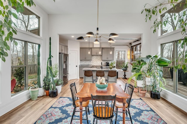 dining room with a high ceiling, sink, a notable chandelier, and light wood-type flooring