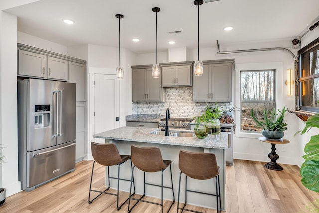 kitchen featuring light stone counters, gray cabinets, high end fridge, and tasteful backsplash