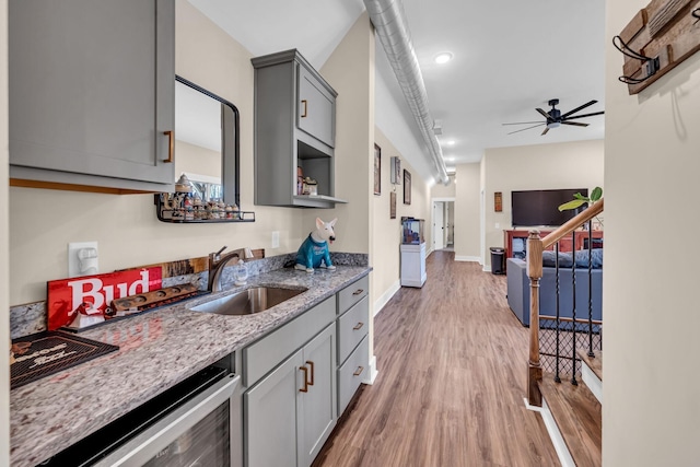 kitchen featuring light hardwood / wood-style floors, light stone countertops, gray cabinetry, sink, and ceiling fan