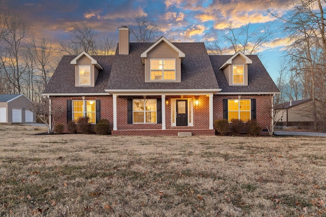 new england style home with covered porch, an outbuilding, a lawn, and a garage