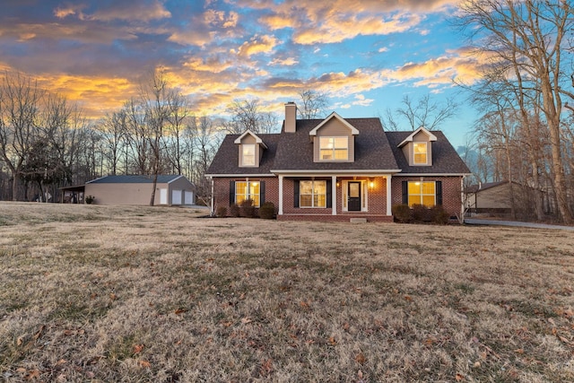 cape cod home with a garage, an outbuilding, a yard, and covered porch