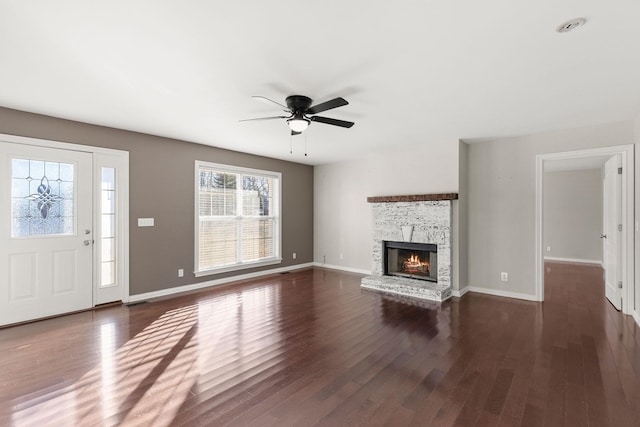 unfurnished living room with ceiling fan, a stone fireplace, and dark hardwood / wood-style flooring