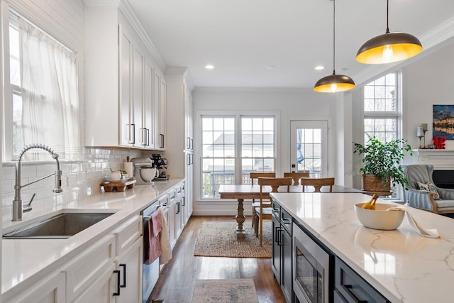 kitchen with hanging light fixtures, sink, white cabinets, light stone countertops, and stainless steel appliances