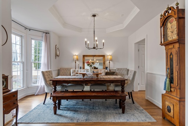 dining area with light wood-type flooring, a raised ceiling, ornamental molding, and a notable chandelier