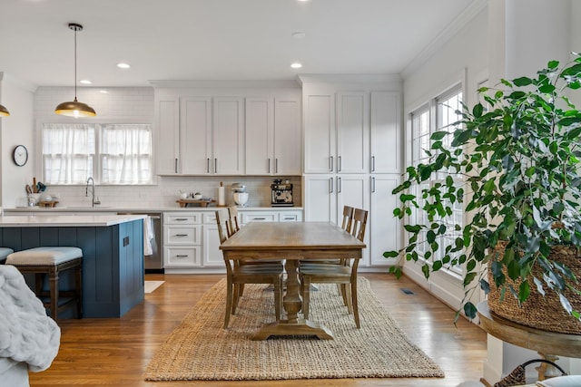 kitchen featuring decorative backsplash, stainless steel dishwasher, white cabinets, decorative light fixtures, and light hardwood / wood-style flooring