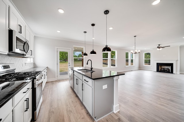 kitchen with appliances with stainless steel finishes, white cabinetry, hanging light fixtures, a kitchen island with sink, and sink