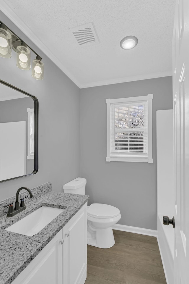 bathroom with a textured ceiling, wood-type flooring, vanity, toilet, and crown molding